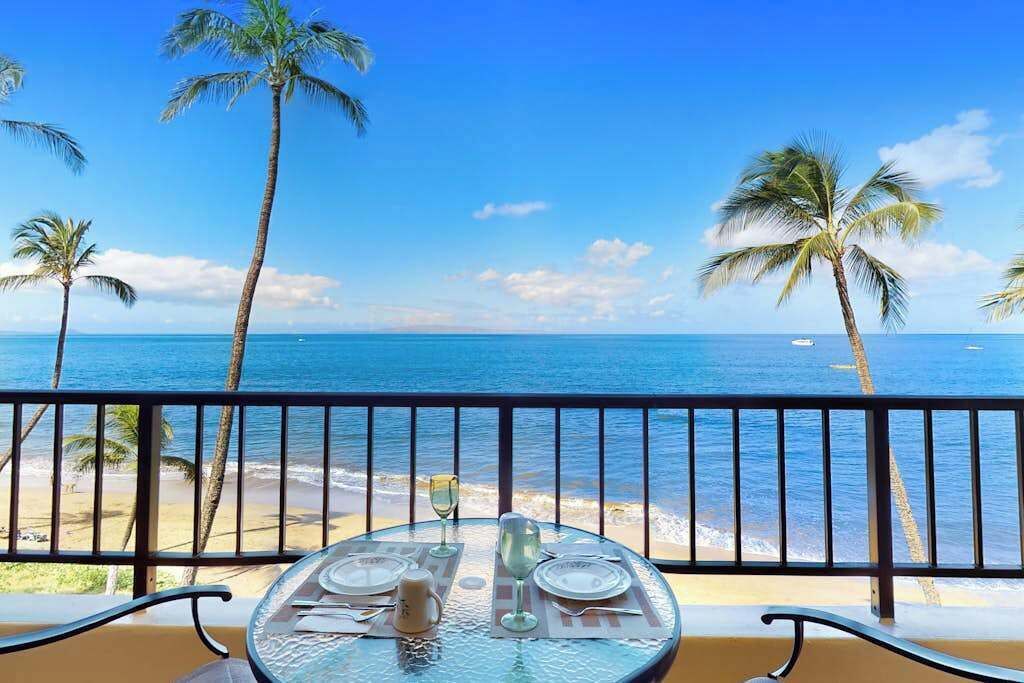 A table set for dining with a view of the ocean and palm trees.