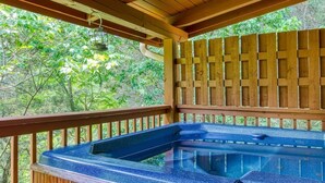 A hot tub with a wooden deck and a view of the surrounding greenery. - Smoky Mountain Hideout (Sevierville)