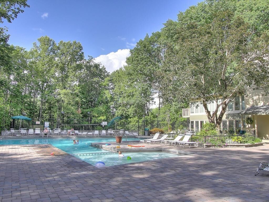 A swimming pool with lounge chairs, a hot tub, and a fenced area with trees.