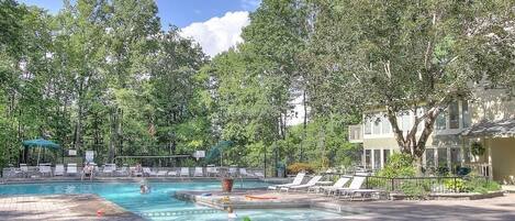 A swimming pool with lounge chairs, a hot tub, and a fenced area with trees.