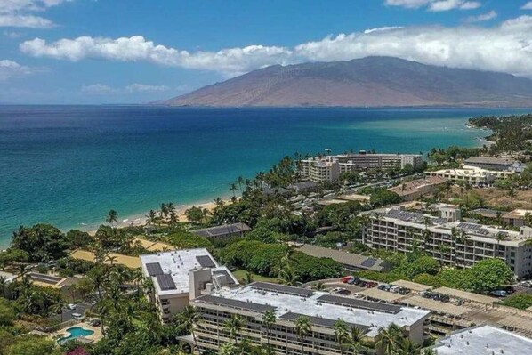 Een kusthotel met meerdere gebouwen, een strand en een berg op de achtergrond.