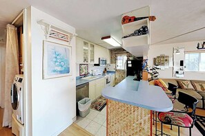 Eine kompakte Küche mit einer zentralen Kochinsel, ein Essbereich mit einer Couch und Stühlen sowie eine kleine Wohnfläche mit Fernseher und Dekorationselementen.