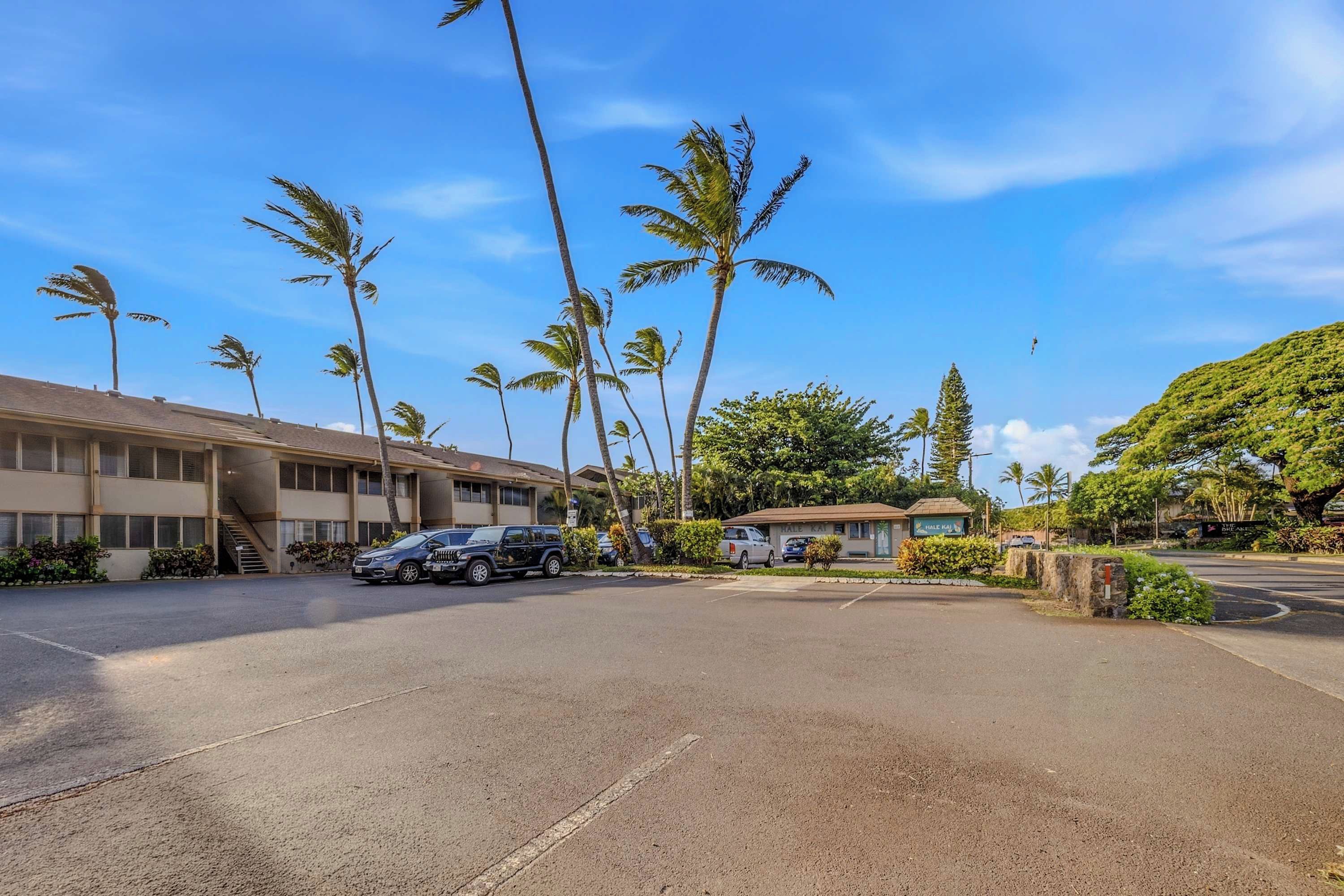 A hotel with a parking lot, several parked cars, and palm trees.