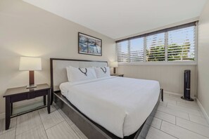 Una habitación de hotel con una cama, mesitas de noche, una ventana con persianas y un cuadro en la pared.