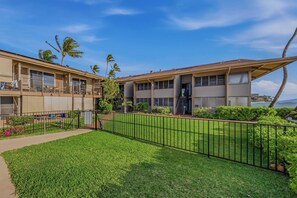 A two-story building with a flat roof, a balcony, and a fenced yard with grass and shrubs. - *NEW* Fall $pecial Ground-Floor Beachfront Lahaina Condo with Pool (Lahaina)