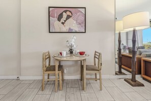 Een eethoek met een tafel, stoelen, een bloemenvaas en een schilderij aan de muur.