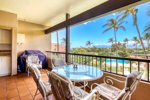 A balcony with a round table and chairs, a grill, and a view of a pool and palm trees. - Maui Kaanapali Royal F303 - Oceanside Resort Villa w/ Pool, Spa, Beach Access (Lahaina)