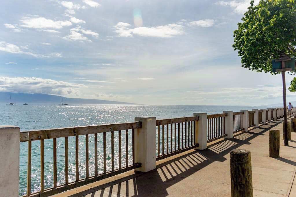 Una passeggiata lungomare con ringhiera in legno, percorso pedonale in cemento e vista aperta sul mare.