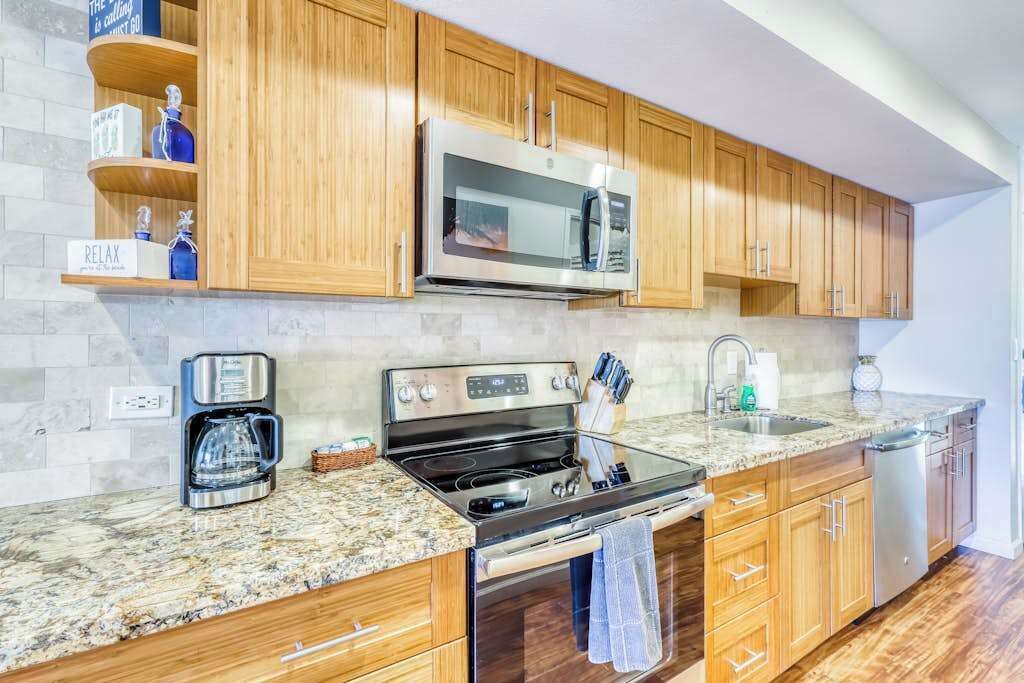 A modern kitchen with wooden cabinets, a stainless steel microwave, a coffee maker, and a sink.