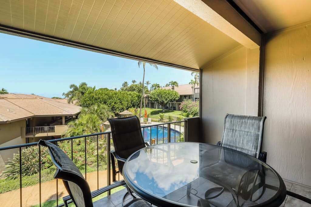 Ein Balkon mit Glastisch und Stühlen, ein Schwimmbad und Blick auf andere Gebäude und Grünflächen.
