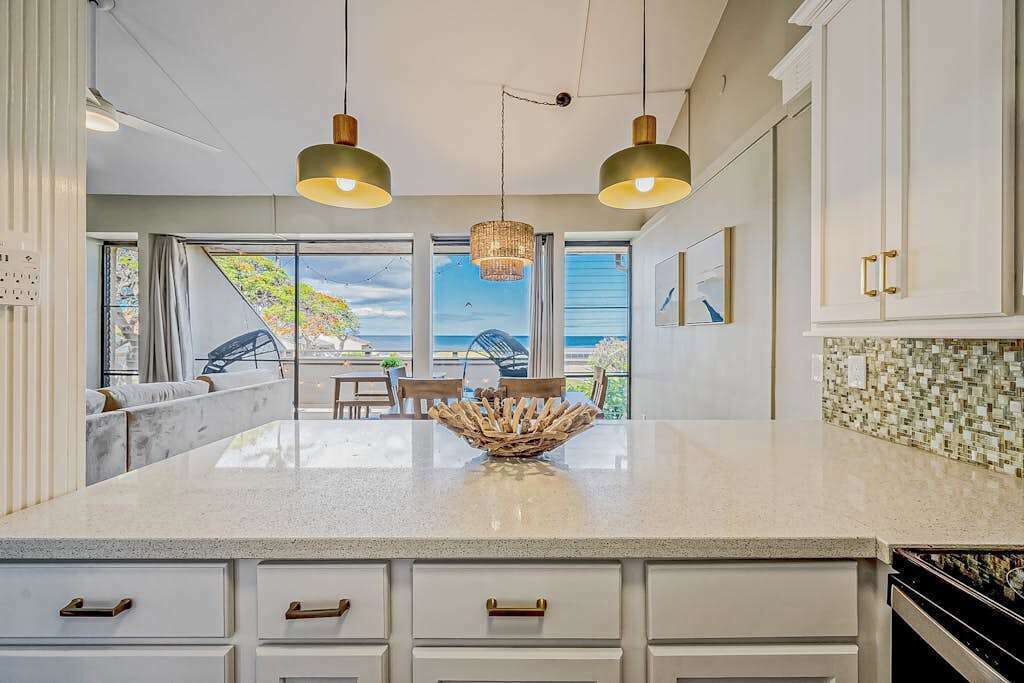 A kitchen with a large island, white cabinetry, pendant lighting, and a view through the window.