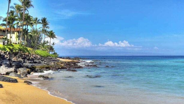 Uma praia com águas azul-claras, areal arenoso e um edifício de telhado vermelho e paredes brancas.