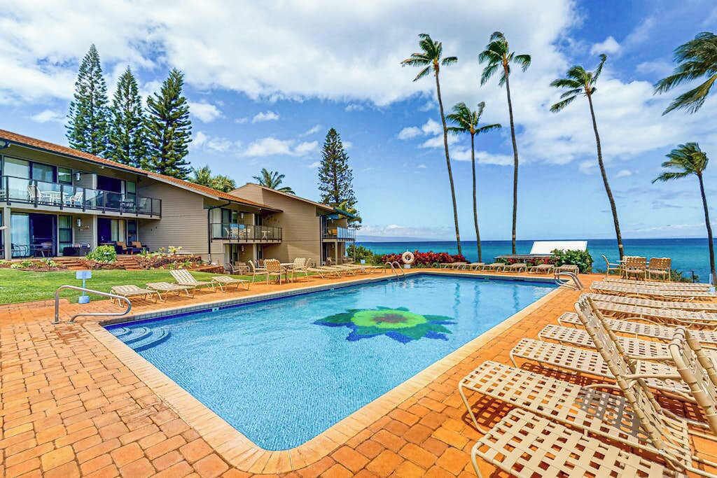 A hotel with a swimming pool, lounge chairs, and a view of the ocean.