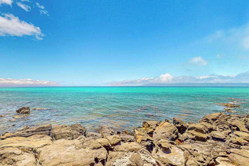 Una costa rocciosa con acque turchesi trasparenti e una catena montuosa all'orizzonte sotto un cielo sereno.