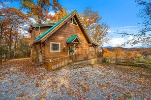A wooden cabin with a green roof, surrounded by trees and a gravel driveway. - Sunrise Pointe (Sevierville)