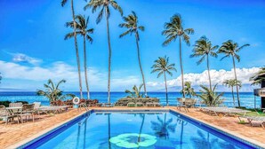 A pool with clear blue water, surrounded by lounge chairs and palm trees, with a view of the ocean. - *NEW* Fall Deal Lofted Ocean View Family Stay at Mahina Surf (Lahaina)