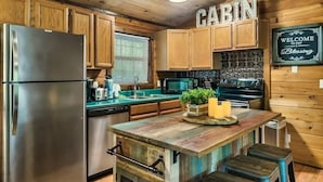 A cabin-style kitchen with wooden cabinets, a stainless steel refrigerator, a microwave, an oven, and a wooden island with stools. - The Blessing Cabin (Sevierville)
