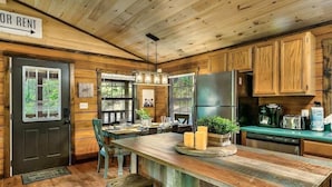 A rustic cabin interior with a wooden dining table, a kitchen area with a refrigerator, and a sign indicating 'FOR RENT'. - The Blessing Cabin (Sevierville)
