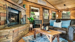 A cozy cabin interior with a stone fireplace, a leather couch, and a sign indicating cabins for rent. - The Blessing Cabin (Sevierville)
