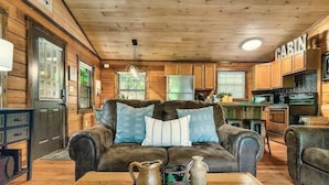 A cozy cabin interior with a leather sofa, wooden walls, a kitchen area, and a dining table with a tray of items. - The Blessing Cabin (Sevierville)