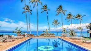 A pool with clear blue water, surrounded by lounge chairs and palm trees, with a view of the ocean. - *New* Fall $pecial Two-Story Oceanfront Views at Mahina Surf (Lahaina)