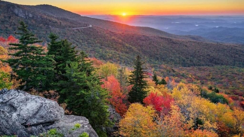 A mountainous landscape with autumn foliage and a sunset.