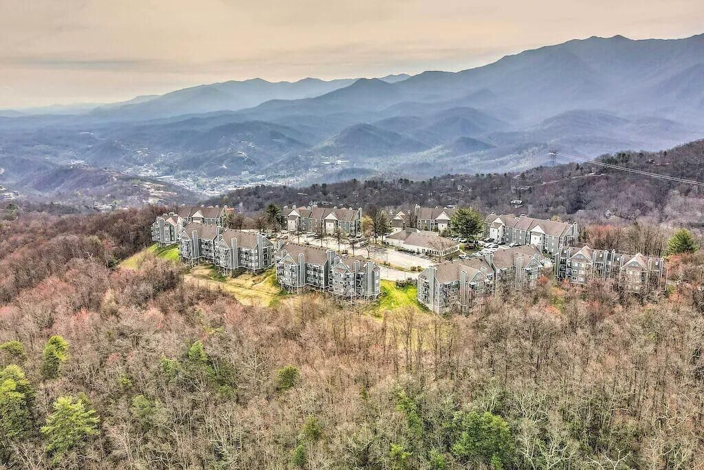 A residential complex with multiple buildings, surrounded by a forested area and mountains in the background.