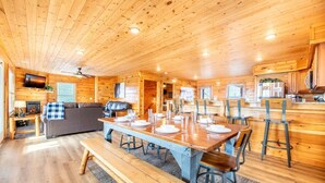 A wooden cabin interior with a dining table set for four, a sofa, and a fireplace. - Time To Unwind (Sevierville)