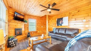 A cozy cabin interior with a fireplace, leather sofa, wooden walls, and a ceiling fan. - Time To Unwind (Sevierville)