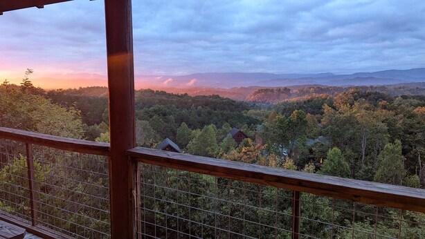 A view from a wooden balcony overlooking a forested landscape with distant mountains. - Time To Unwind (Sevierville)
