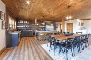A modern kitchen with wooden flooring, a central island, bar stools, and a dining table with chairs. - Top of the Summit Lodge (Sevierville)