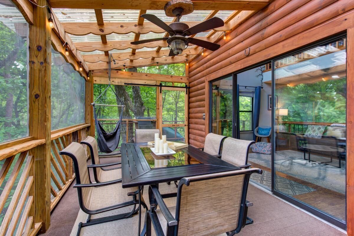 A wooden cabin with a glass-enclosed patio, a dining table with chairs, and a ceiling fan.