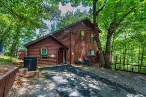 A rustic log cabin with a front porch, a small attached structure, and a gravel driveway. - Z - Treehouse Overlook (Sevierville)