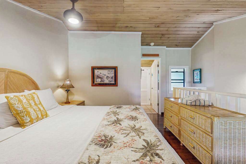Un dormitorio con cama, mesita de noche, lámpara, cómoda y puerta que da a otra habitación.