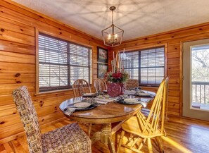 A wooden interior with a dining table set for four, surrounded by wicker chairs, and large windows with blinds. - Twin Mountain (Sevierville)