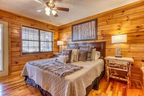 A wooden-paneled bedroom with a bed, two bedside lamps, a ceiling fan, and a window with blinds. - Twin Mountain (Sevierville)