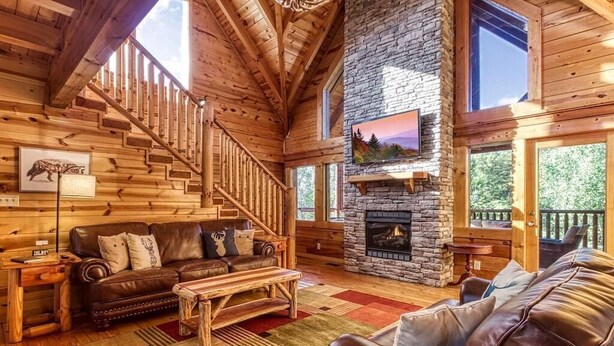 L’intérieur d’une cabane en rondins, avec une cheminée en pierre, un escalier en bois et un canapé en cuir.