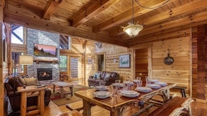 L’intérieur d’un chalet rustique, avec une cheminée en pierre, une table à manger en bois, un canapé en cuir et un coin chaleureux autour du foyer.