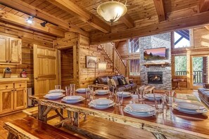 A wooden cabin interior with a dining table set, a fireplace, a staircase, and a stone wall. - Z - Uncle Buck's Cabin (Pigeon Forge)