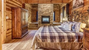 Une chambre située dans une cabane en rondins, avec une cheminée en pierre, des meubles en bois et un ventilateur de plafond.