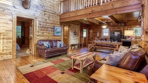 L’intérieur d’une cabane en rondins, avec un plafond en bois, une cheminée, un canapé en cuir et un coin repas.