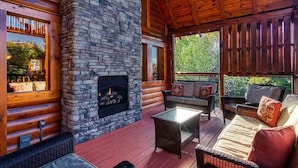 L’intérieur d’une cabane en rondins, avec une cheminée en pierre, des murs en bois et une véranda dotée de sièges d’extérieur.