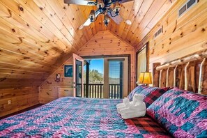 A wooden cabin bedroom with a bed, a chandelier, and a balcony. - Z - Walden's Creek Lodge (Sevierville)