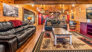 L’intérieur d’une cabane en rondins, avec un canapé en cuir, une table basse en bois et un escalier menant à une mezzanine.