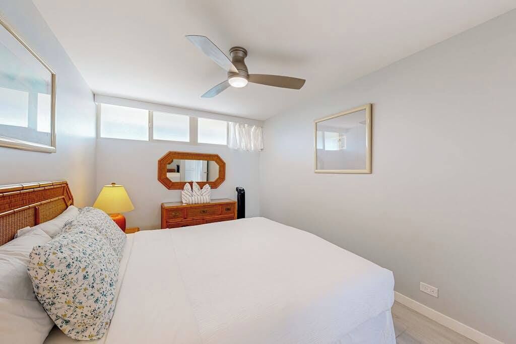 A bedroom with a bed, a ceiling fan, a nightstand, a lamp, a dresser, and a mirror.