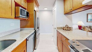 Una cocina con armarios de madera, electrodomésticos de acero inoxidable, encimera de granito y vista al área de estar.