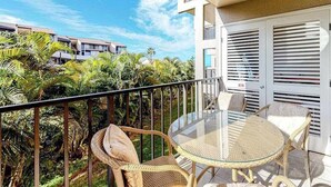Ein Balkon mit Rattanmöbeln, einem Glastisch und Blick auf einen tropischen Garten.