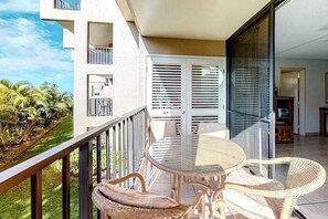 Ein Balkon mit einem Glastisch und Korbstühlen, mit Blick auf einen Garten und ein Gebäude.