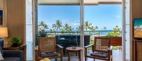 A room with a balcony, two wicker chairs, a small table, a sofa, and a TV.