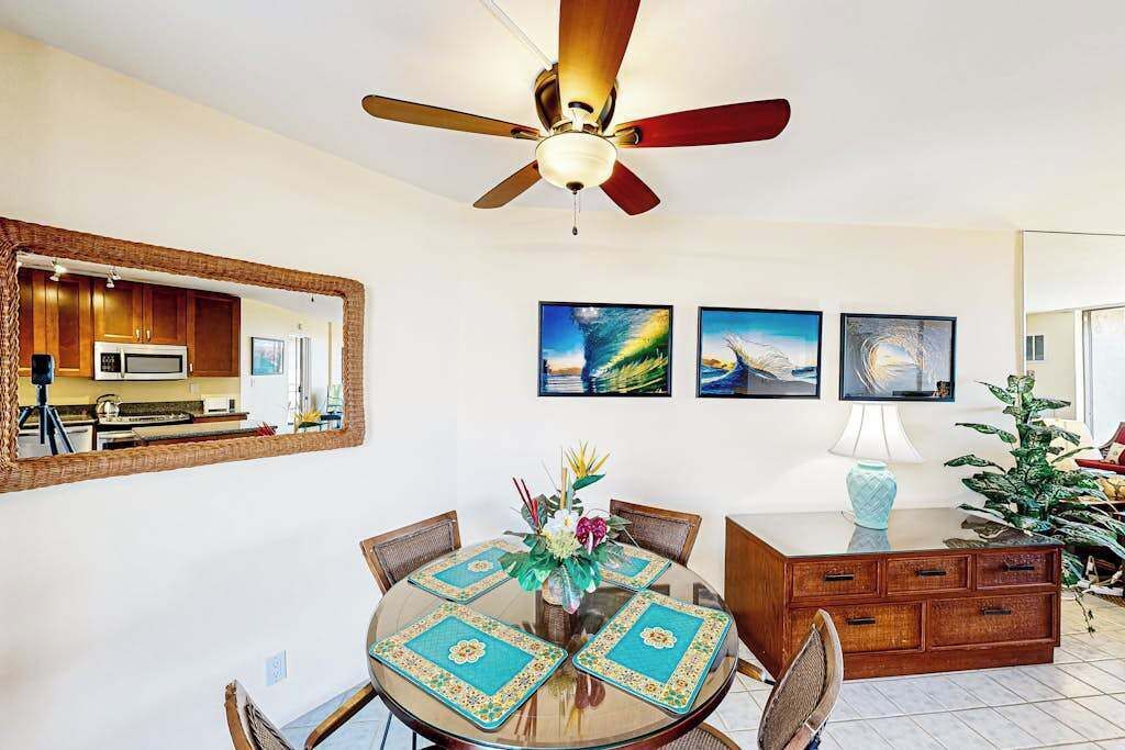 A dining area with a round table, chairs, a ceiling fan, a mirror, and artwork on the wall.